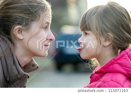 Close up portrait of young mom and her daughter girl making faces to each other outdoors. Close up portrait of young mom and her daughter girl making faces to each other outdoors. 113871163