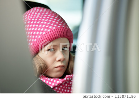 Sad child girl in warm knitted winter clothes outdoors. 113871186
