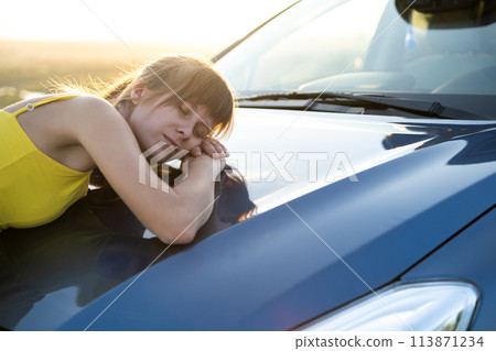 Carefree woman driver in yellow summer dress enjoying warm evening near her car. Travel and vacation concept. Carefree woman driver in yellow summer dress enjoying warm evening near her car. Travel and vacation concept. 113871234