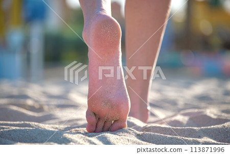 Close up of female feet walking barefoot on white grainy sand of golden beach on blue ocean water background Close up of female feet walking barefoot on white grainy sand of golden beach on blue ocean water background 113871996