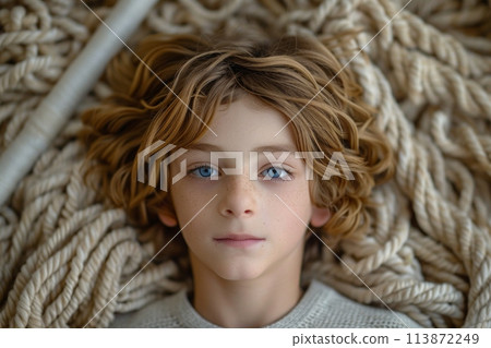 A young boy with messy hair lays relaxed on top of a chaotic pile of rope, lost in his thoughts. 113872249