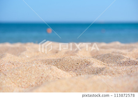 Close up of clean yellow sand surface covering seaside beach with blue sea water on background. Travel and vacations concept. Close up of clean yellow sand surface covering seaside beach with blue sea water on background. Travel and vacations concept. 113872578