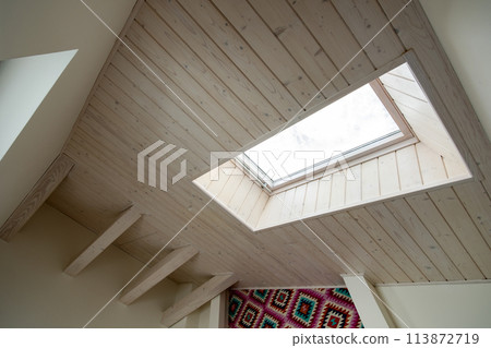 Wooden ceiling in a contemporary mansard room with attic window ob decorative planks surface. Wooden ceiling in a contemporary mansard room with attic window ob decorative planks surface. 113872719