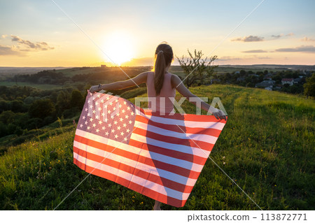 Back view of happy young woman posing with USA national flag outdoors at sunset. Positive girl celebrating United States independence day. International day of democracy concept. 113872771