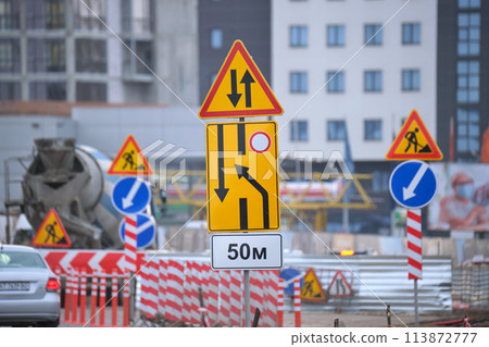 Roadworks warning traffic signs of construction work on city street and slowly moving cars Roadworks warning traffic signs of construction work on city street and slowly moving cars 113872777