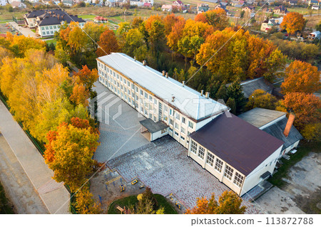 Aerial view of school, college or kindergarten building with big yard among autumn trees on rural landscape background 113872788