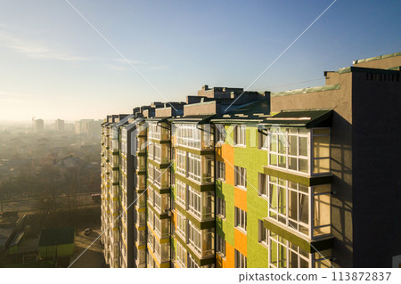 Aerial view of a tall residential apartment building with many windows and balconies. Aerial view of a tall residential apartment building with many windows and balconies. 113872837