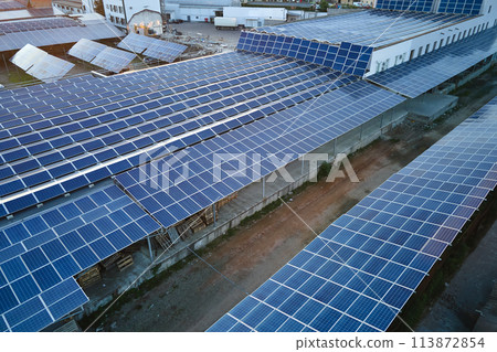 Aerial view of solar power plant with blue photovoltaic panels mounted on industrial building roof for producing green ecological electricity. Production of sustainable energy concept 113872854