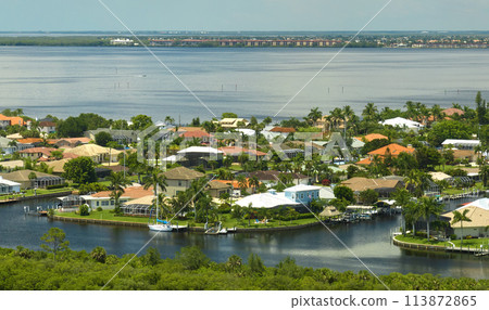 Aerial view of residential suburbs with one storey houses located near wildlife wetlands with green tropical vegetation on sea shore. Living close to nature in warm climate concept Aerial view of residential suburbs with one storey houses located near wildlife wetlands with green tropical vegetation on sea shore. Living close to nature in warm climate concept 113872865