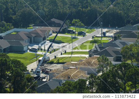 Professional builders and crane truck working on roof construction of unfinished suburban home with wooden frame structure in Florida rural area. Concept of housing development in America 113873422