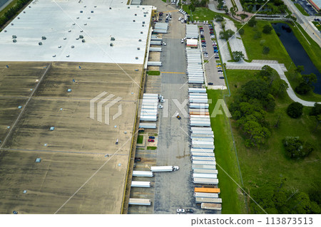 Aerial view of large commercial loading bay with many delivery trucks unloading and uploading retail goods for nationwide distribution. Global economy concept 113873513