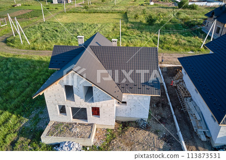 Aerial view of unfinished house with aerated lightweight concrete walls and wooden roof frame covered with metallic tiles under construction 113873531