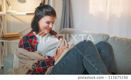Diary leisure. Creative writer. Home weekend. Happy inspired woman writing story in journal relaxing on comfy couch at cozy room interior. 113875298