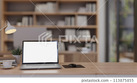 The wooden table showcases a computer in a contemporary office with a bookshelf in the background. The wooden table showcases a computer in a contemporary office with a bookshelf in the background. 113875855