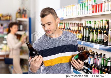 Interested man making purchases in grocery store, buying bottle beer Interested man making purchases in grocery store, buying bottle beer 113876288