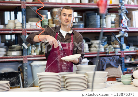 Young man paints blanks of ceramic products Young man paints blanks of ceramic products 113876375