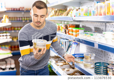 Adult man chooses pickled herring in store 113876530