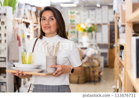 Latino woman holding purchases and walking in household goods store Latino woman holding purchases and walking in household goods store 113876711