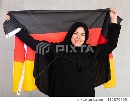 smiling Muslim woman in traditional black hijab holds flag of Germany smiling Muslim woman in traditional black hijab holds flag of Germany 113876869