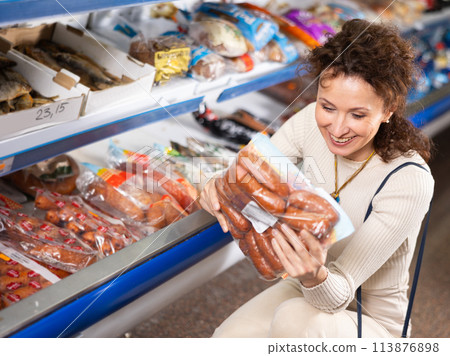 Adult woman chooses sausages in store Adult woman chooses sausages in store 113876898