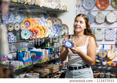 Female buyer holds in hands tests wall plate in memorable gifts shop 113877033
