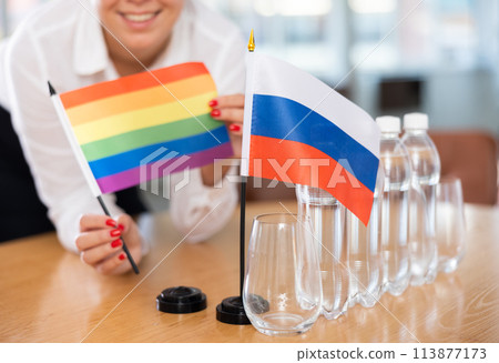 Young woman puts LGBT and Russia flags on table in office 113877173