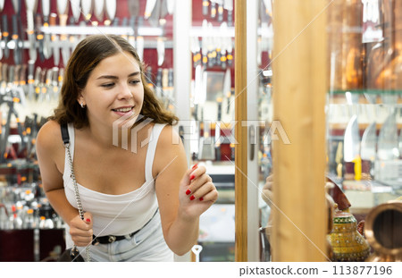 Interested young woman viewing copper utensil placed on display case Interested young woman viewing copper utensil placed on display case 113877196