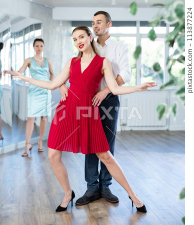 Woman in red dancing passionate bachata with man at dance class Woman in red dancing passionate bachata with man at dance class 113877224