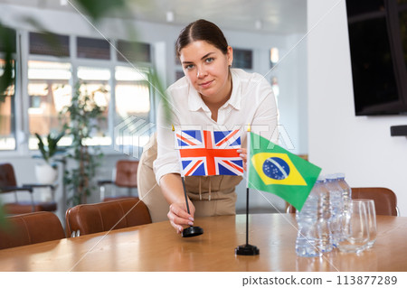 Young female assistant putting up brazilian and british flags on table for international negotiations 113877289