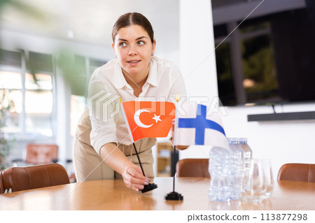Young female assistant putting up finnish and turkish flags on table for international negotiations 113877298