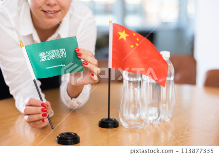 Unrecognizable girl sets midget flags of China and Saudi Arabia before international negotiations 113877335