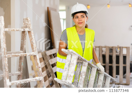 Portrait of woman in protective yellow vest and hard hat in room being renovated 113877346