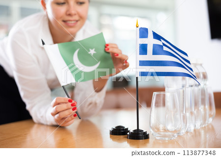 Employee of delegation prepares negotiating table - sets up flag of Greece and Pakistan 113877348