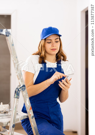 Cheerful young female builder using phone at construction site 113877387