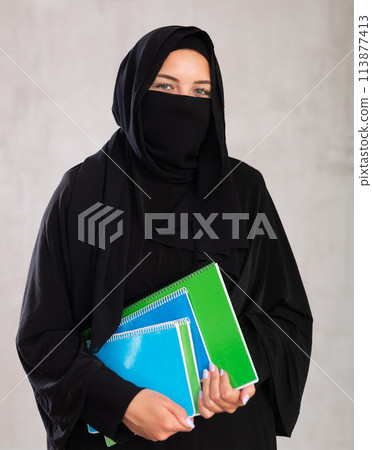 girl with face covered with burka holds lot of thick notebooks. foreign girl with face covered with burka holds lot of thick notebooks. foreign 113877413