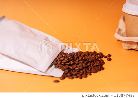 Paper cup in tray next to whole coffee beans on orange background 113877482