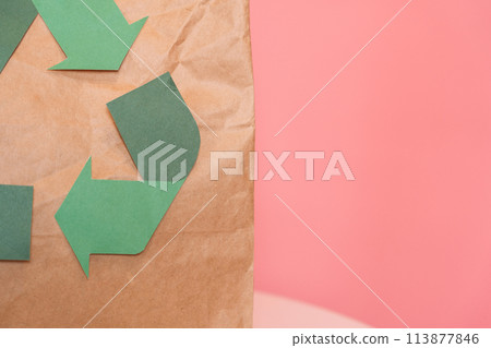 Paper bag with recycling sign with old clothes on table in front of pink background 113877846