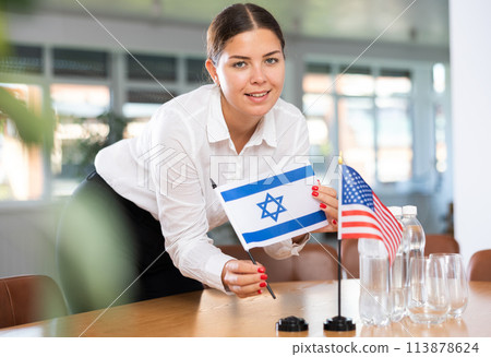 Young woman puts flags of Israel and USA on table in office Young woman puts flags of Israel and USA on table in office 113878624