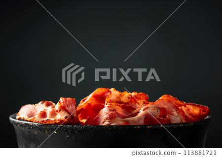 Fried bacon slices in old black pan. Fried bacon slices in old black pan. 113881721