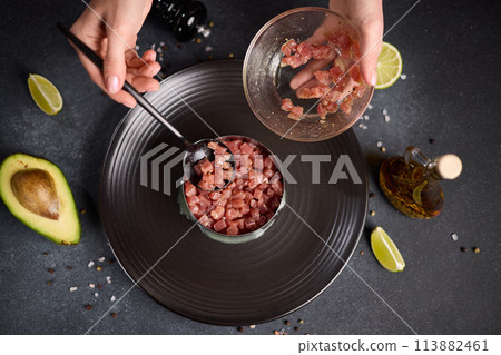 Tuna and avocado tartare recipe - woman fills cooking form with sliced chopped tuna fillet Tuna and avocado tartare recipe - woman fills cooking form with sliced chopped tuna fillet 113882461