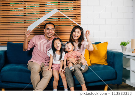 A joyful family enjoys the warmth of their cozy living room holding a cardboard roof mockup symbolizing protection and planning during their home relocation. Safety and togetherness is the answer. 113883333