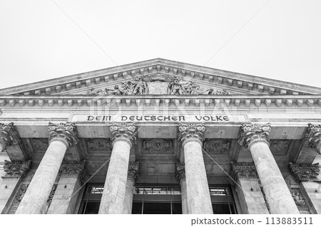 The monochrome facade of the Reichstag building, showcasing its iconic pillars and inscription: Dem Deutschen Volke. The seat of the German Bundestag, Berlin, Germany.. Black and white image. The monochrome facade of the Reichstag building, showcasing its iconic pillars and inscription: Dem Deutschen Volke. The seat of the German Bundestag, Berlin, Germany.. Black and white image. 113883511