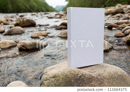 white paper with the empty cover perched on the stones of a river. 113884375