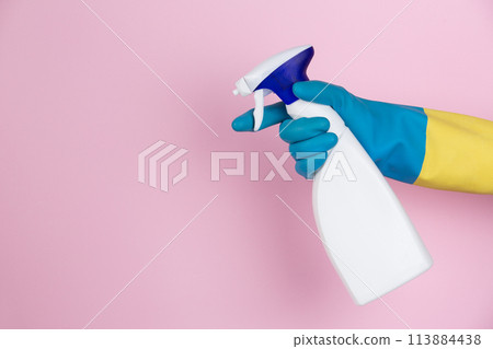 A hand with cleaning gloves squeezing a spray bottle on a pink background 113884438