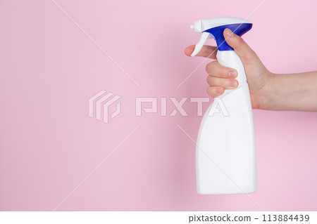 A woman hand squeezing a spray bottle on a pink background 113884439