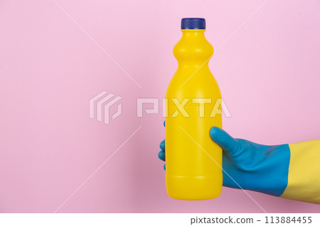 A hand with cleaning gloves holding a bottle of bleach on a pink background A hand with cleaning gloves holding a bottle of bleach on a pink background 113884455