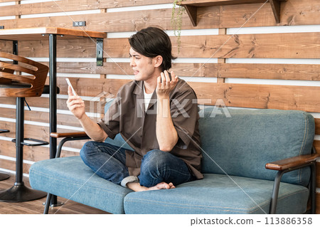 一個年輕人在家放鬆時玩智慧手機（遇到麻煩、回覆、發電子郵件、擔心、迷失） 113886358