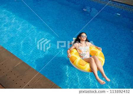 Happy teenage girl relaxing in inflatable ring in swimming pool, view from above Happy teenage girl relaxing in inflatable ring in swimming pool, view from above 113892432