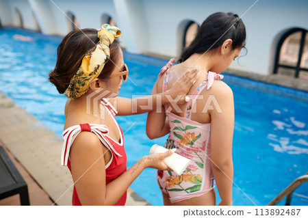 Mother applying sunscreen on back of teenage daughter 113892487