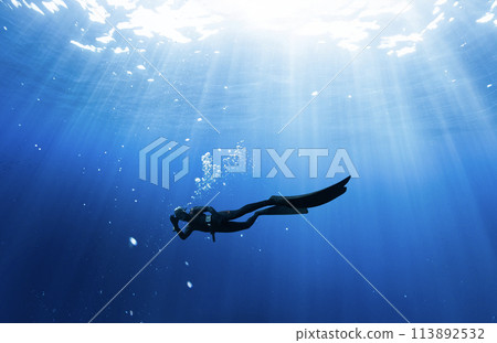 Freediver Swimming in Deep Sea With Sunrays. Freediver Swimming in Deep Sea With Sunrays. 113892532